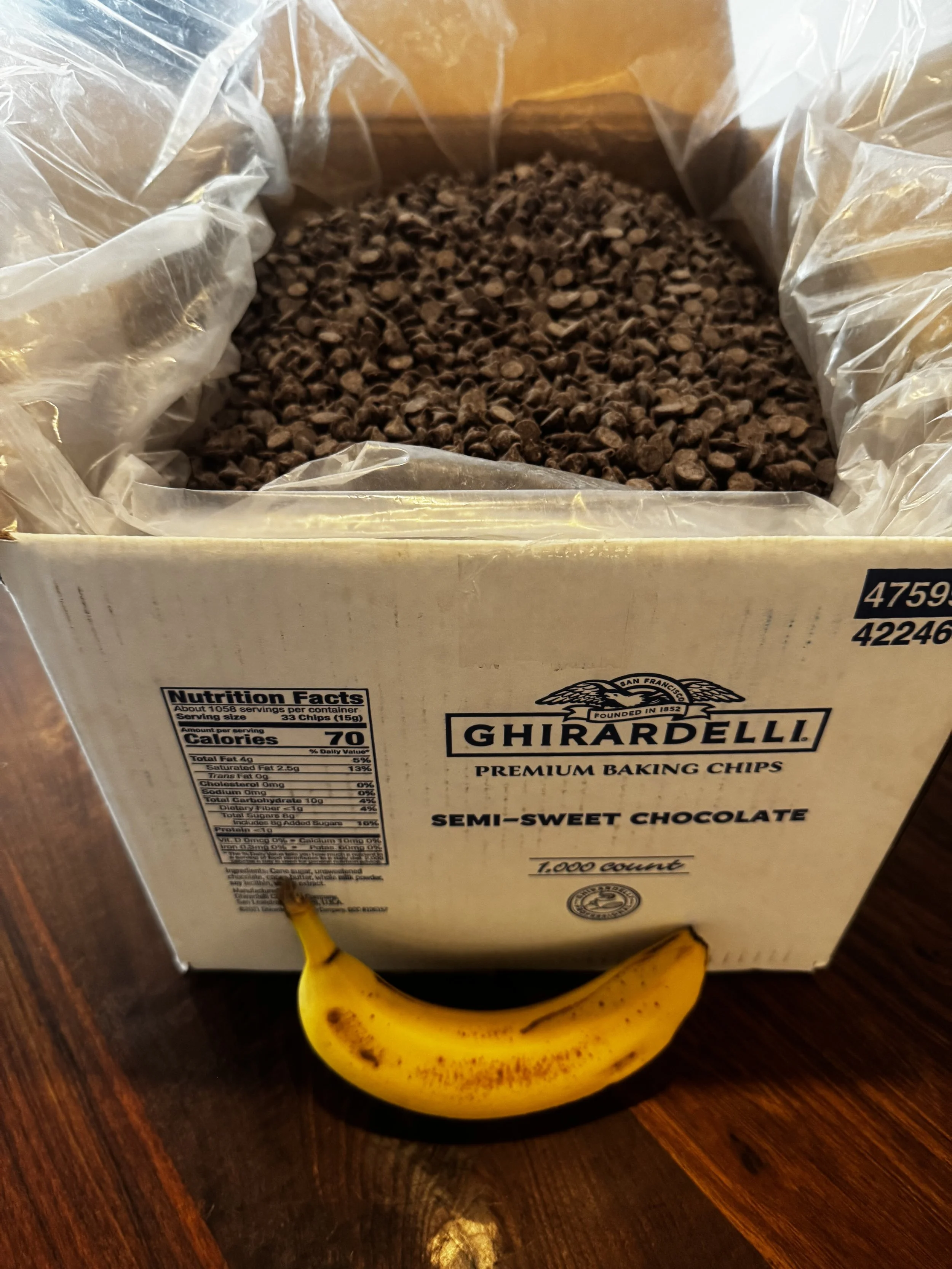 A box of Ghirardelli semi-sweet chocolate baking chips with a banana in front of it on a wooden surface.
