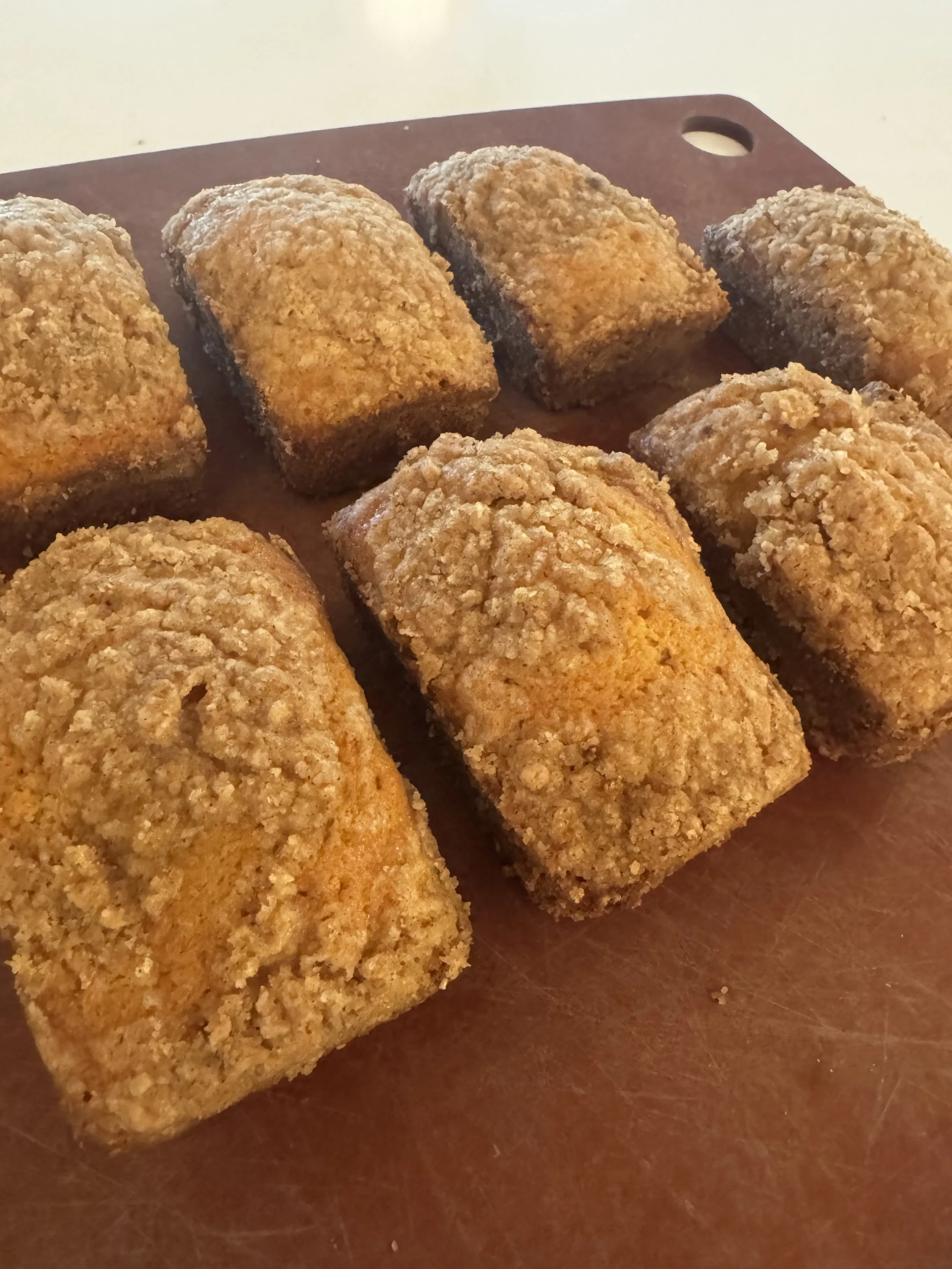 Six golden-brown, breaded, fried croquettes on a brown cutting board.
