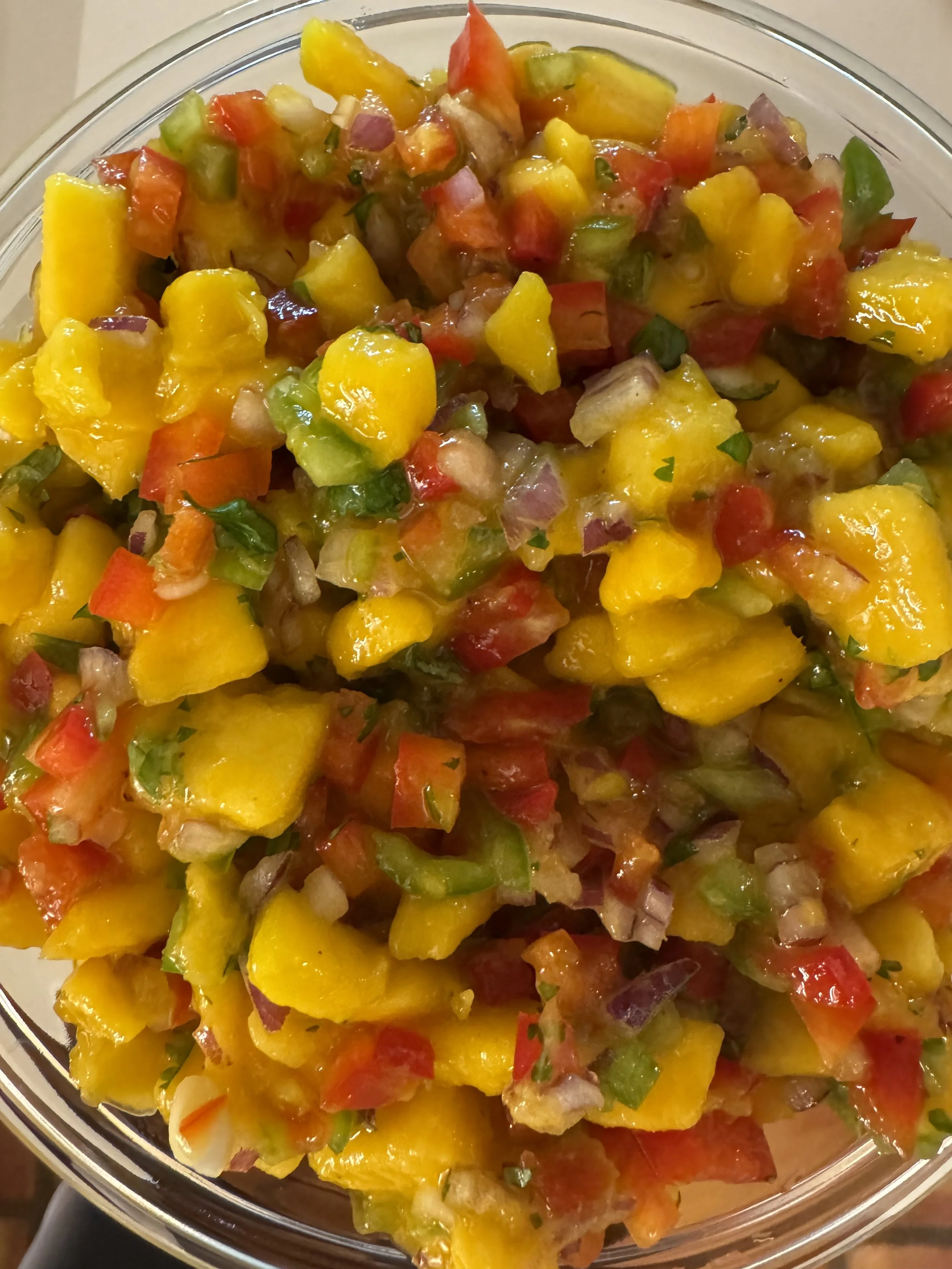 A bowl of freshly chopped mango salsa with diced red and green tomatoes, onions, and cilantro.