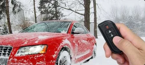 Red car with snow and ice on it, being remotely unlocked with a key fob in snowy outdoor setting.