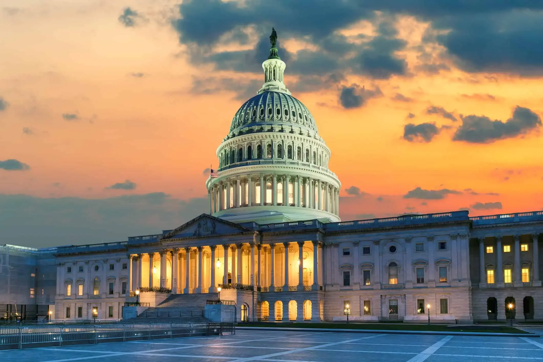 The United States Capitol building at sunset with a cloudy sky and illuminated windows.