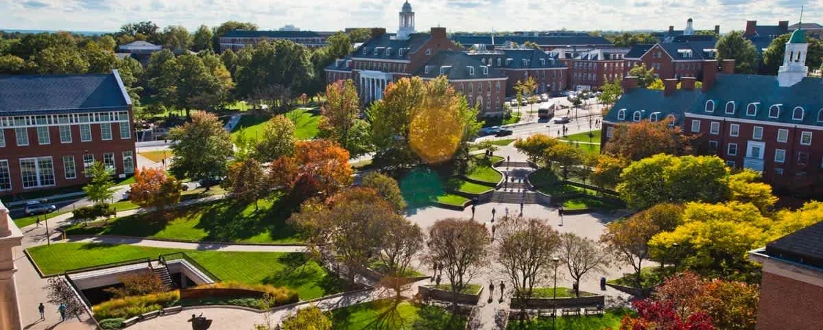 Aerial view of a college campus with brick buildings, green trees, and a central courtyard with walkways and benches.