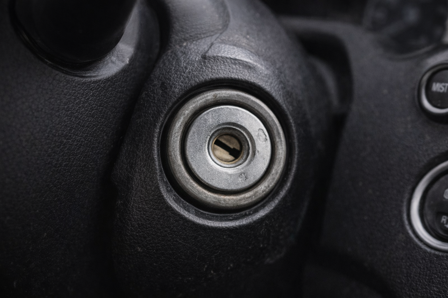 Close-up of a car ignition switch without a key, showing the metal key slot surrounded by a textured black dashboard.