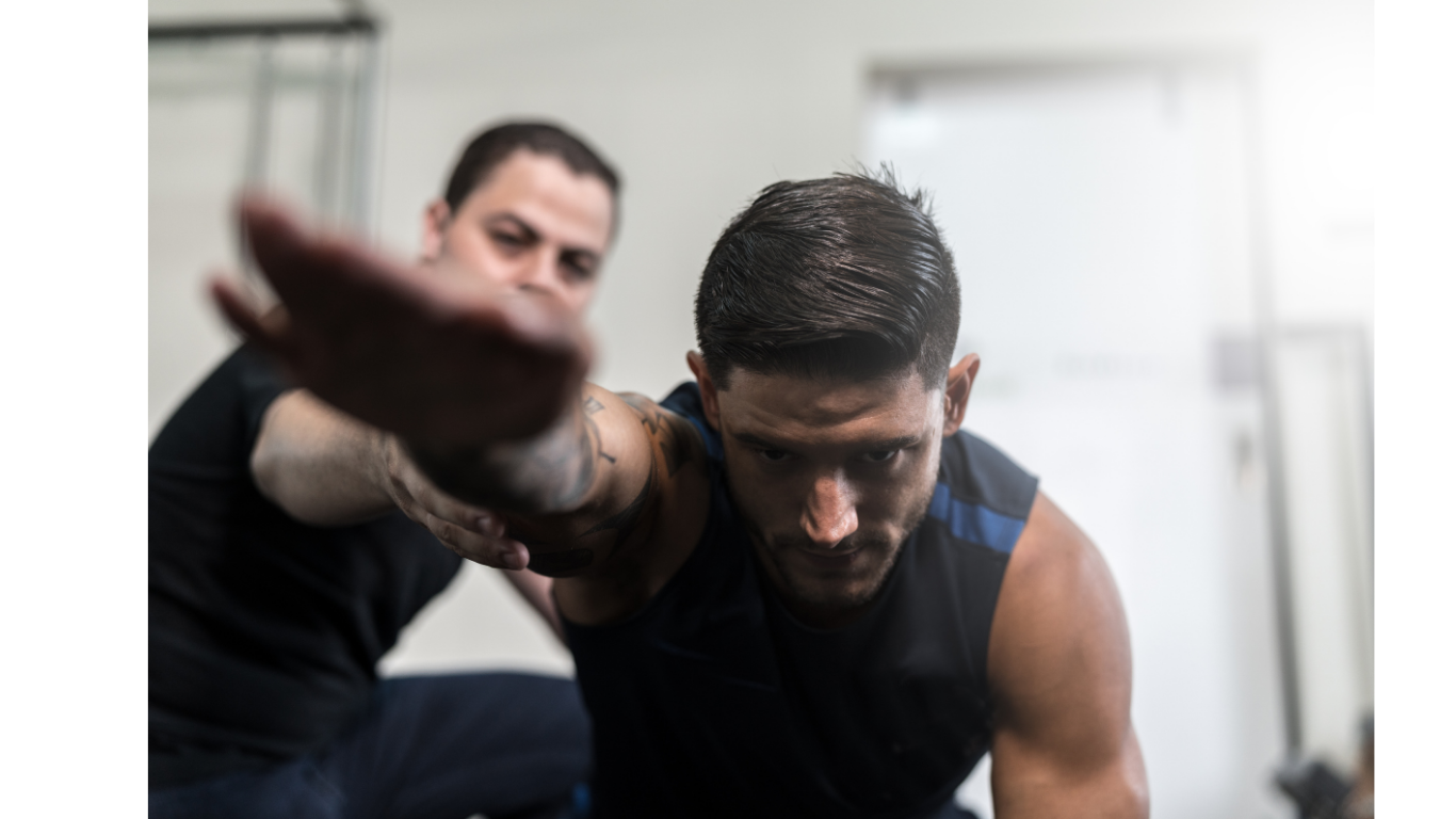 A personal trainer assisting a man with stretching or physical therapy in a gym or fitness center.