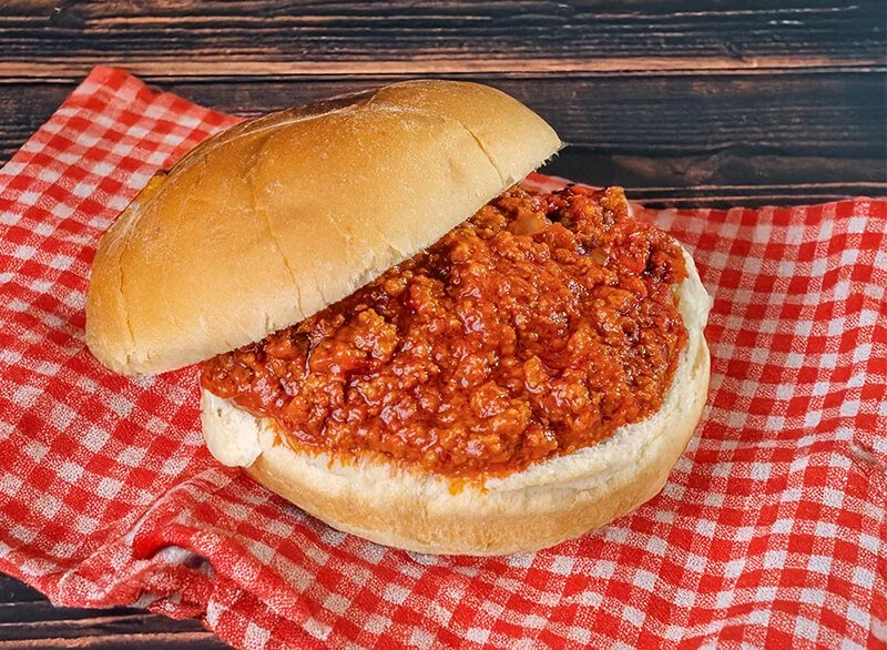 Chili served in a sandwich bun on a red and white checkered napkin.