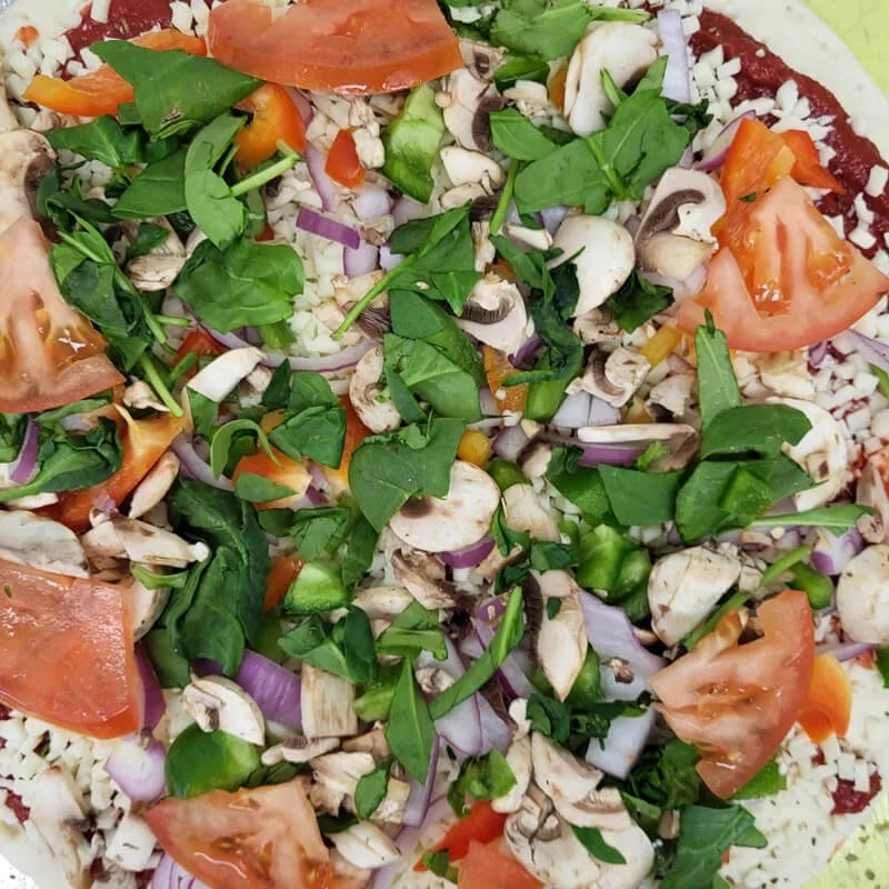 A close-up of fresh vegetable salad with chopped tomatoes, green basil, sliced mushrooms, red onions, green peppers, and shredded cabbage.