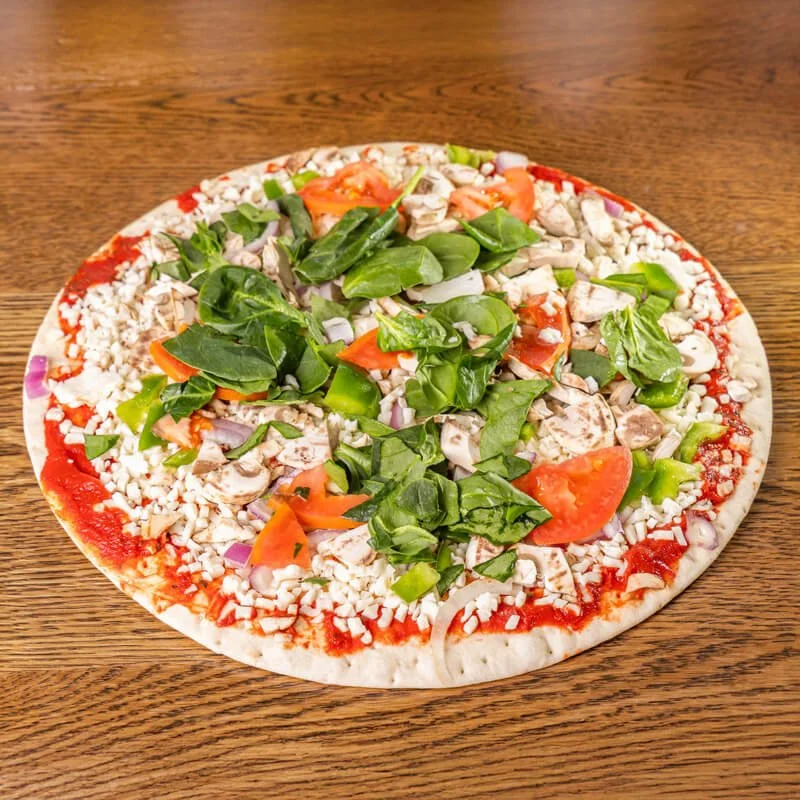 Unbaked pizza with tomato sauce, shredded cheese, chopped tomatoes, green peppers, spinach, and onions on a wooden table.