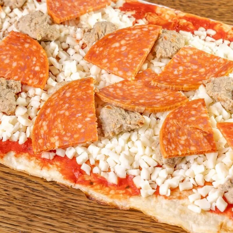 Close-up of a pizza with slices of pepperoni, chunks of sausage, and shredded cheese on a wooden surface.