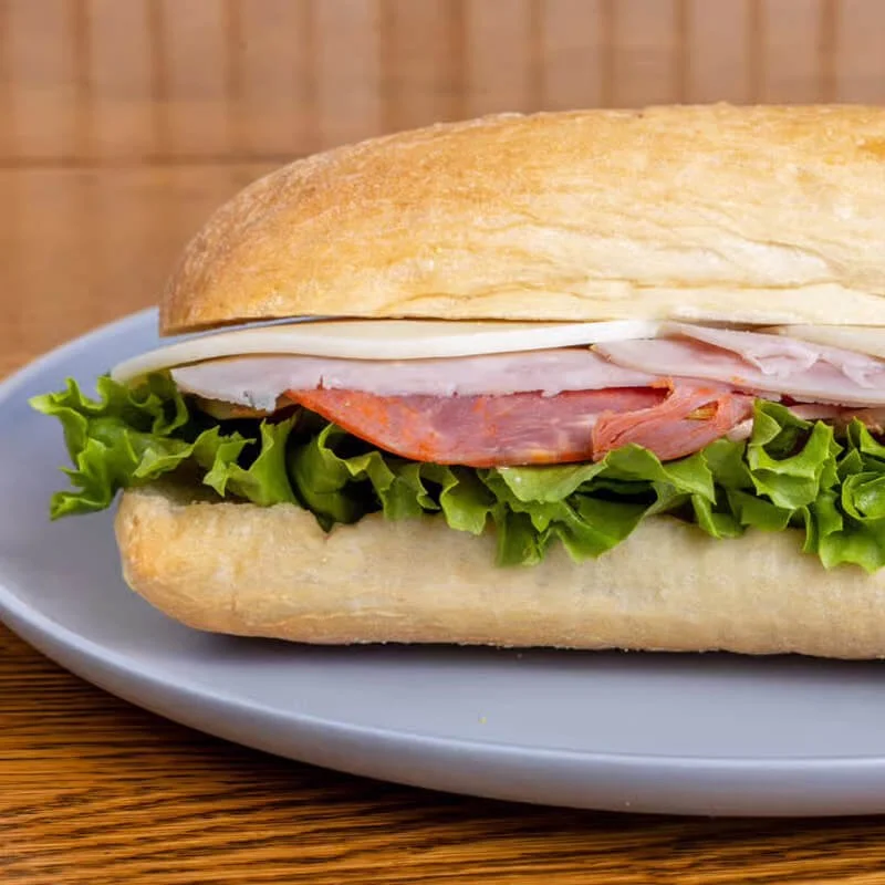 A sandwich with lettuce, turkey, ham, and cheese on a baguette roll served on a white plate.