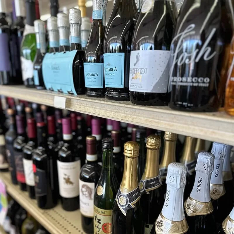 Rows of wine and champagne bottles on store shelves, including sparkling wine with foil tops and various still wines with labels.