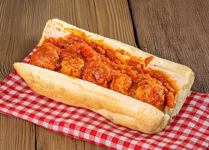 Hot meatball sub sandwich in a hoagie bun with marinara sauce on a red and white checkered cloth