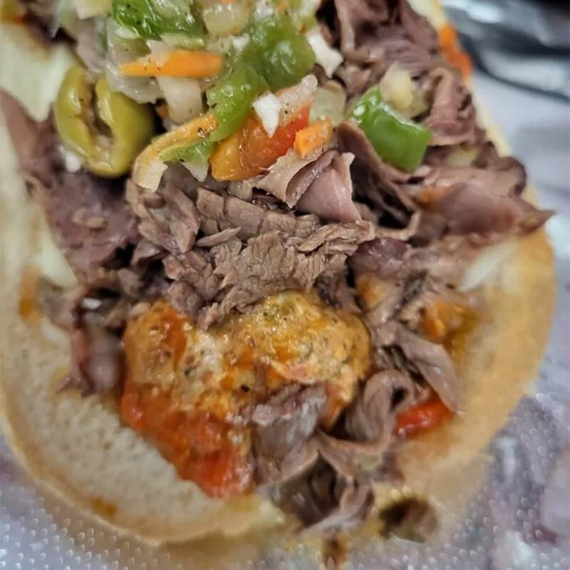 Close-up of a taco filled with shredded beef, cheese, chopped green and orange peppers, and topped with diced tomatoes and lettuce.