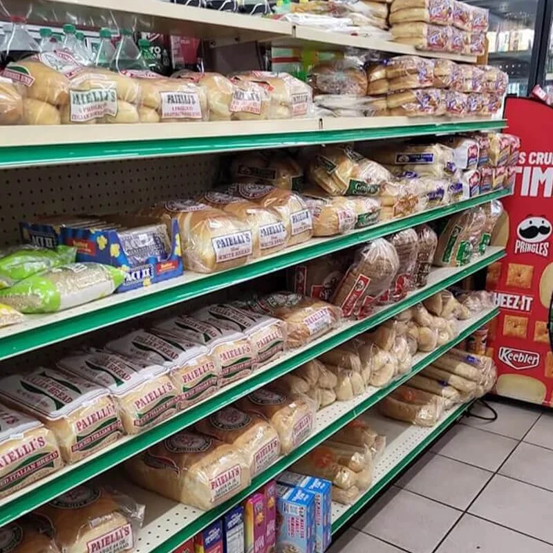 Multiple shelves stocked with various types of bread in a grocery store. There are packages labeled 'Paelli's' and other bread brands, with some smaller packaged bread and bread rolls on the lower shelves.