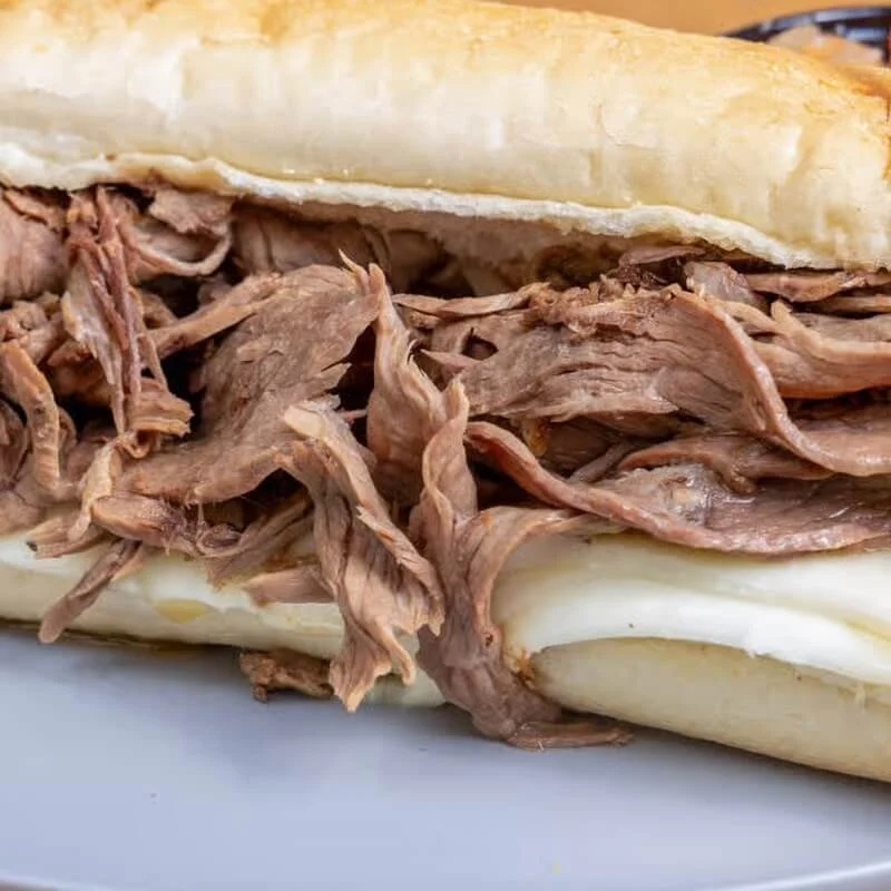 Close-up of a sandwich with shredded cooked beef on a bun.