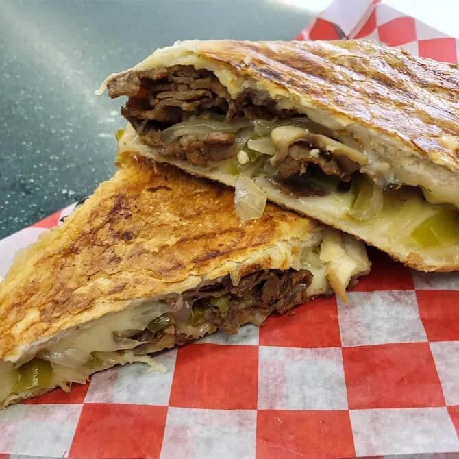 A grilled sandwich cut in half showing melted cheese, cooked onions, mushrooms, and cooked beef inside.