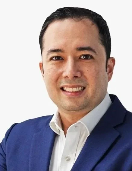 Portrait of a man in a navy blue suit with a white shirt, smiling against a plain light background.