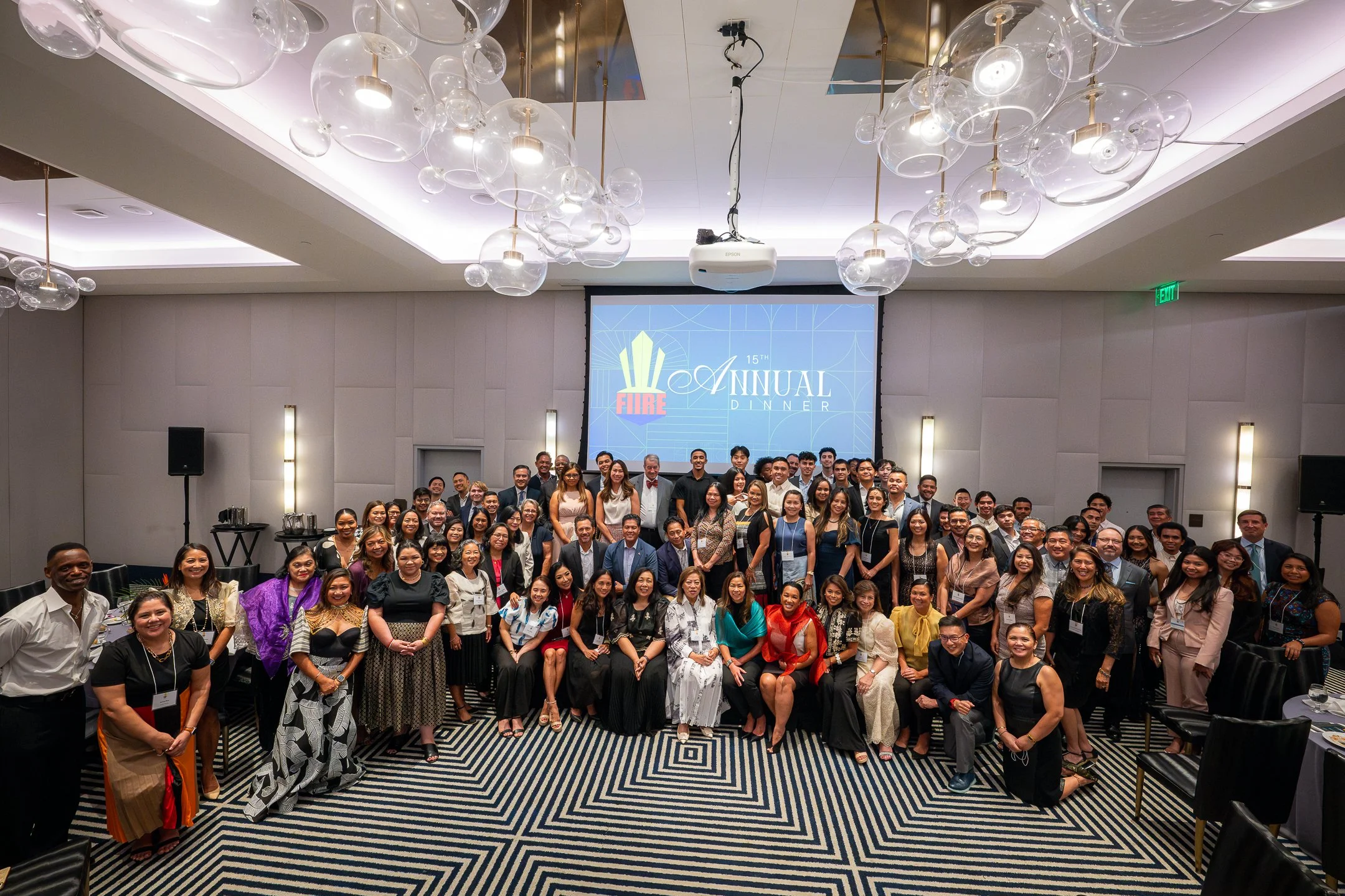 Large group of people posing for a photo at a formal event, with a screen in the background reading '15th Annual Dinner' and a logo with the word 'FIRE'.