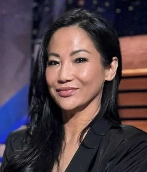 A woman with long black hair, wearing a black top, smiling slightly, in a professional setting.