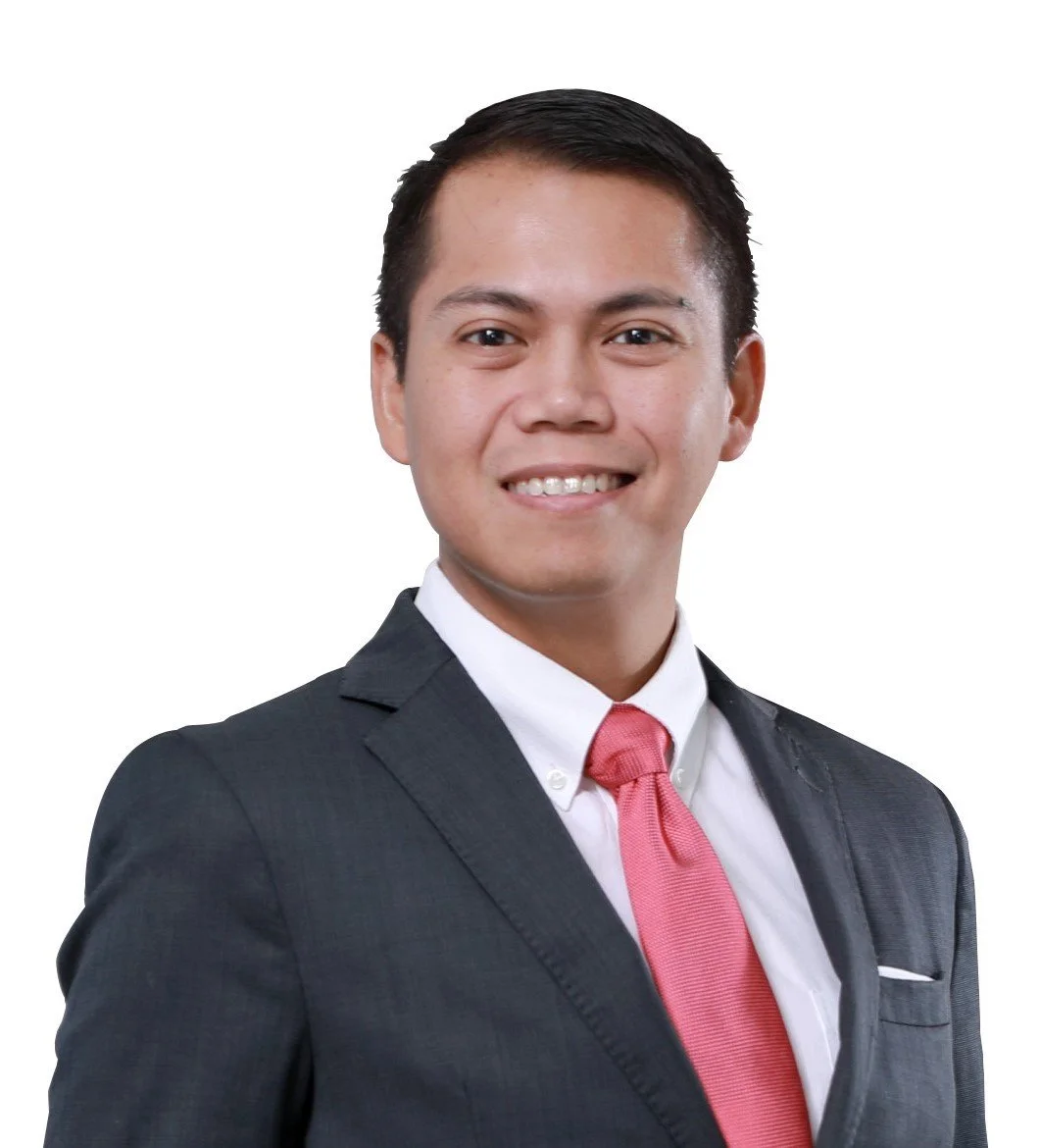Portrait of a smiling man in a dark suit, white shirt, and pink tie against a white background.