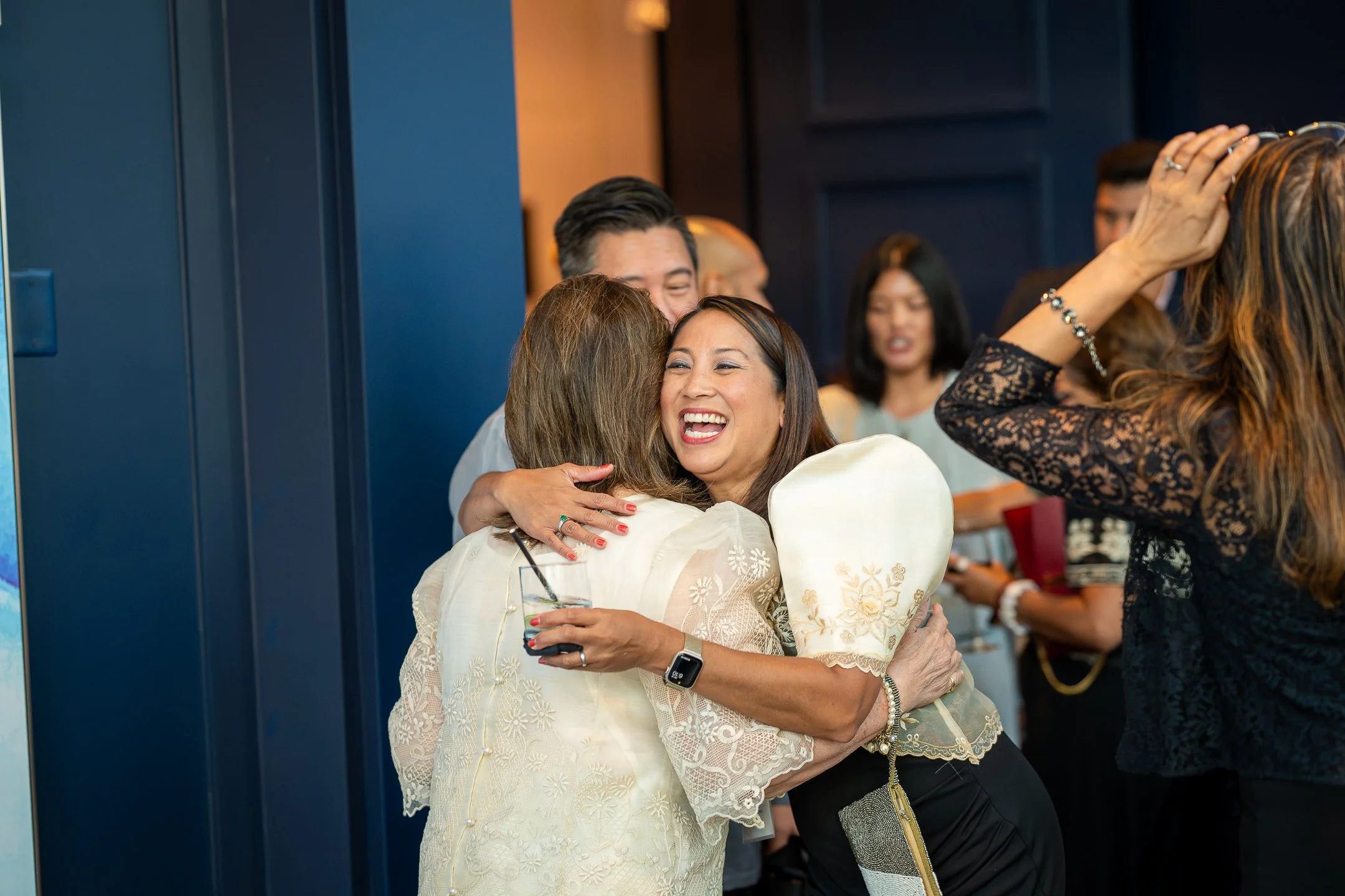 People hugging and celebrating at a social gathering, woman smiling broadly hugging another woman