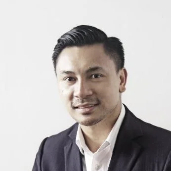 A young man in a dark suit and white shirt smiling in a professional portrait.