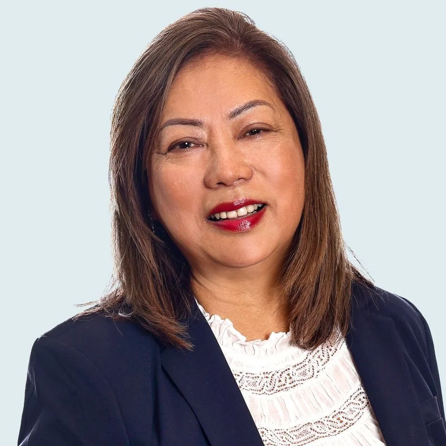 A professional woman with shoulder-length brown hair, wearing a dark blazer over a white lace blouse, smiling slightly against a light background.