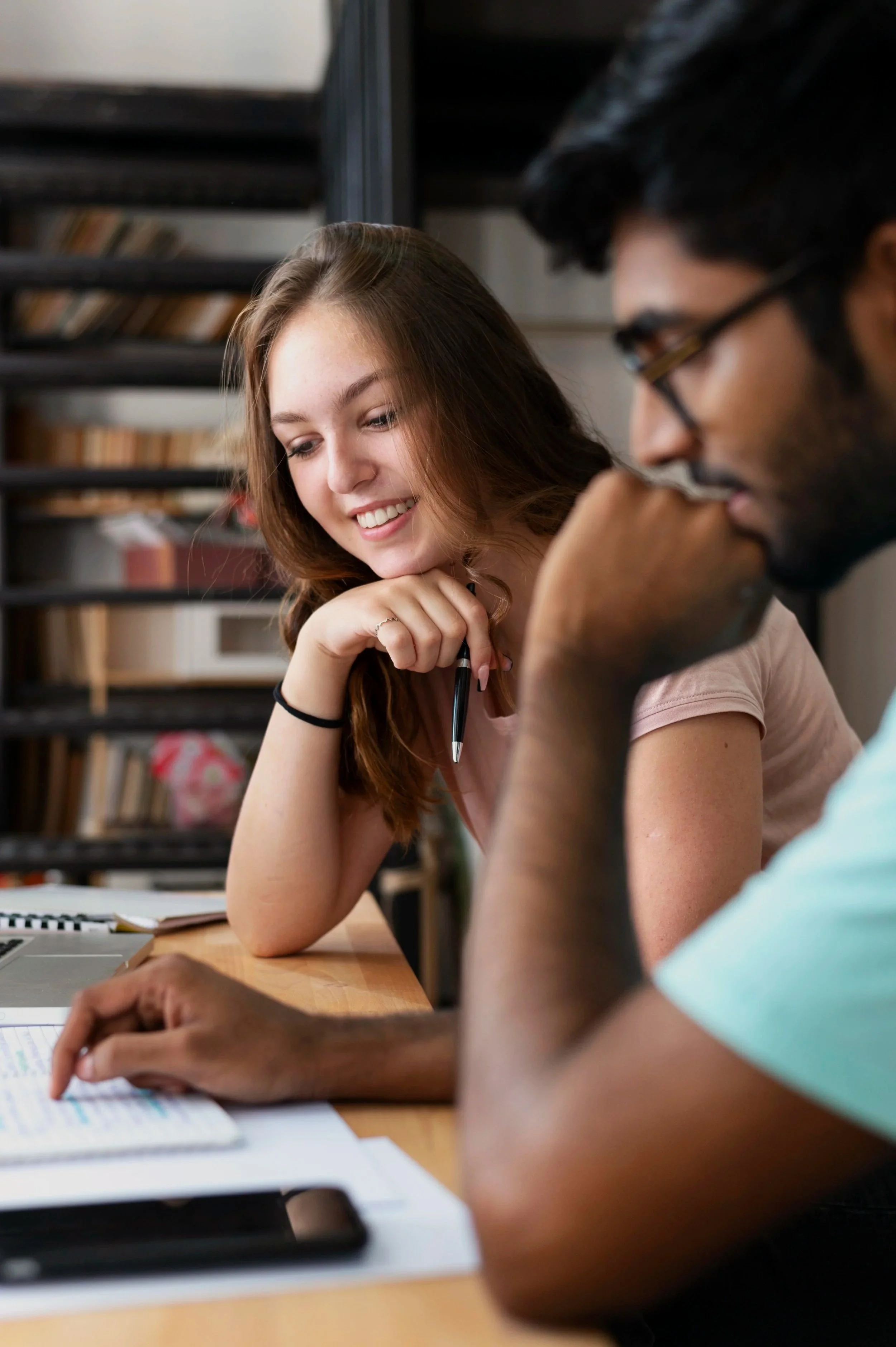 A young woman smiling and chatting with a young man during a study session at a library.