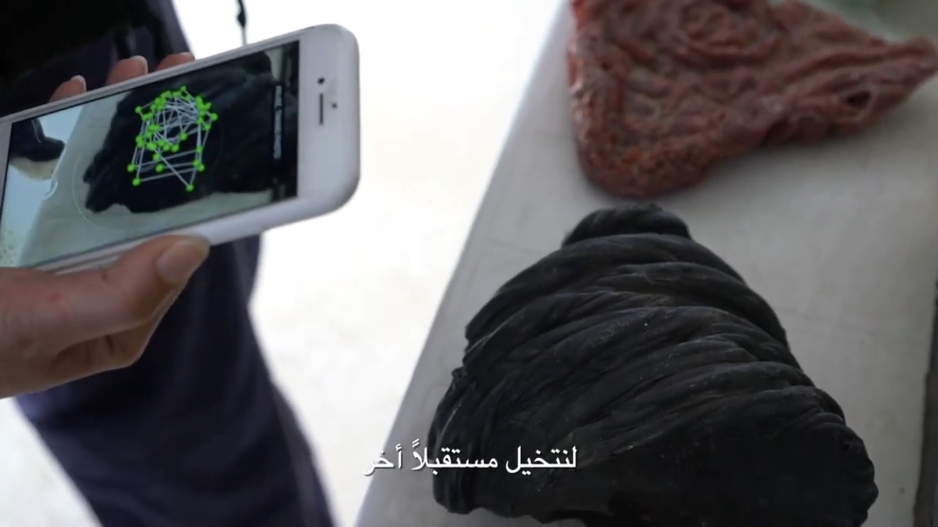 Person holding a smartphone displaying a 3D model with green dots and lines, with a rock and a large coiled black object on a white surface in the background, an artwork by Huniti Goldox.