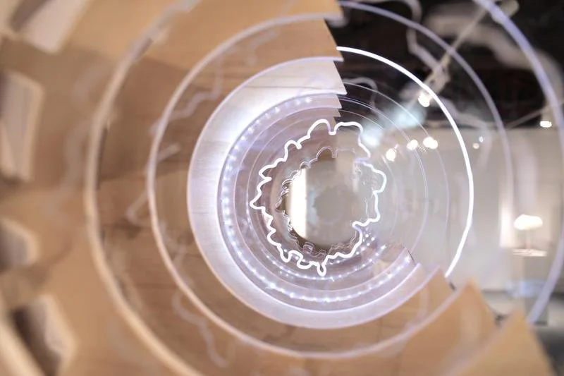 Overhead view of a modern glass staircase with LED lighting, representing the time rings of a tree, created by artist Yuqing Liang.