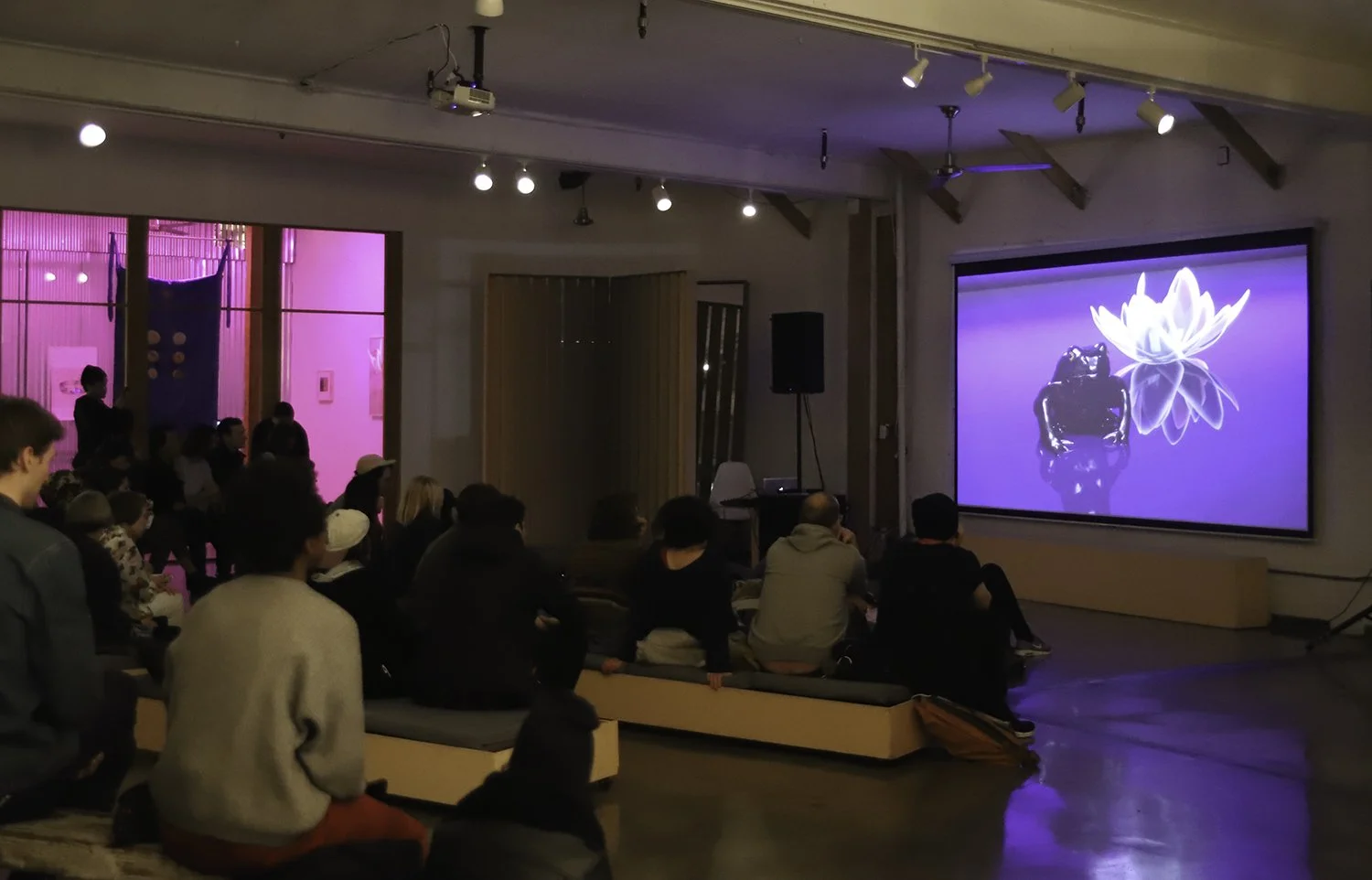 People sitting on benches at Navel in Los Angeles, watching a video by Sofia Albina Novikoff Unger, projected on a large screen in a dimly lit room at Navel in Los Angeles.