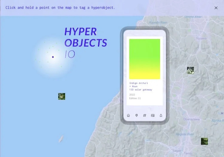 A digital map with a smartphone displaying a hyperobject and the text 'HYPEROBJECTS'. The background shows a map of a region with rivers and terrain, and there are small images of natural landscapes scattered across the map.