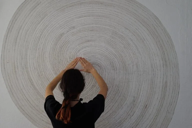 Artist Elisa Balmaceda practicing meditation in front of a circular, concentric line art on a wall.