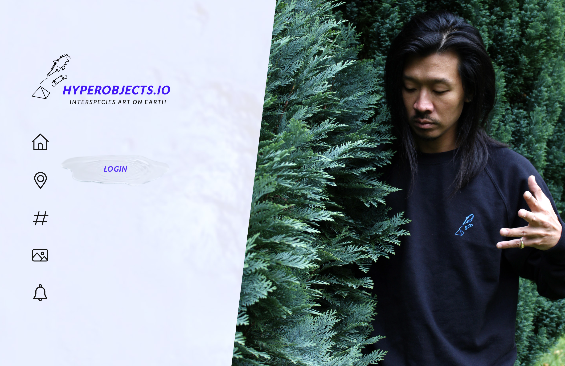 Dancer and massage therapist Ardian Hartono with long dark hair wearing a black shirt with a blue logo, standing outdoors and communicating with a large evergreen bush.