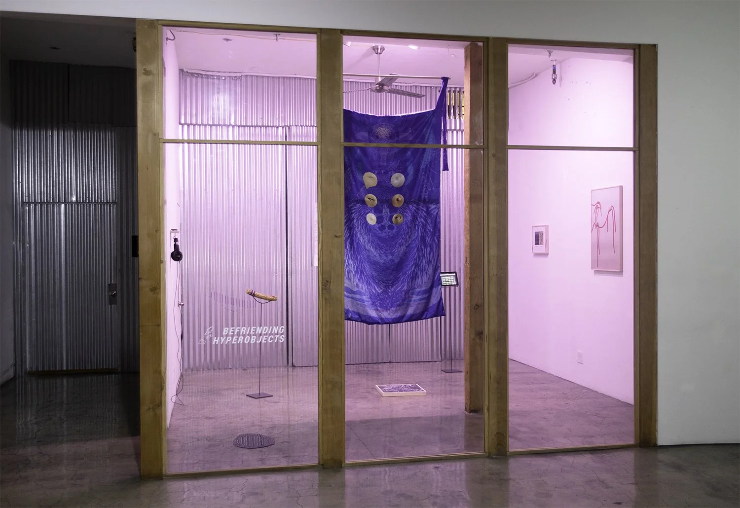 The first group exhibition "Befriending HyperObjects" at Navel in Los Angeles. The space has pink lighting and a small digital screen on a stand in the center.