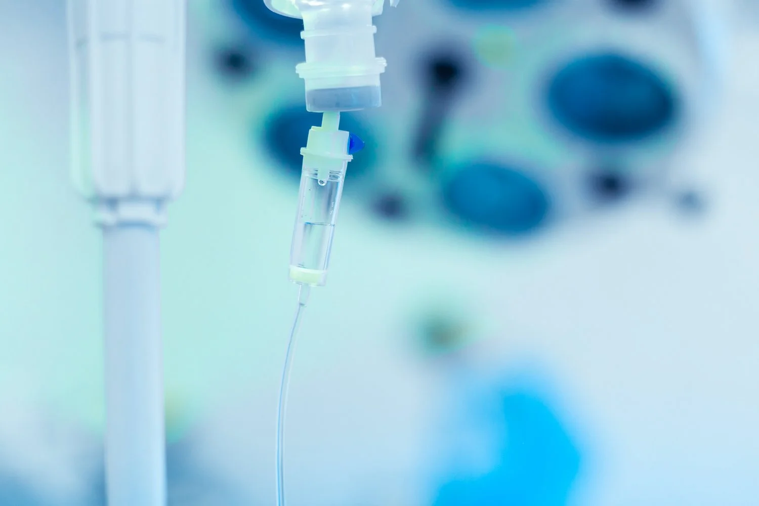 Close-up of an intravenous (IV) drip in a hospital setting with a clear fluid inside the IV bag and tubing, in a clinical environment.