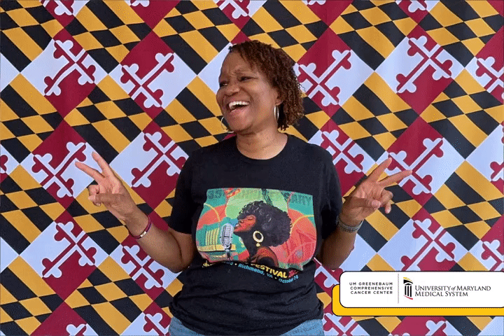 A happy woman gives the peace sign and poses in-front of a Maryland Flag backdrop for Side-A's boomerang booth.