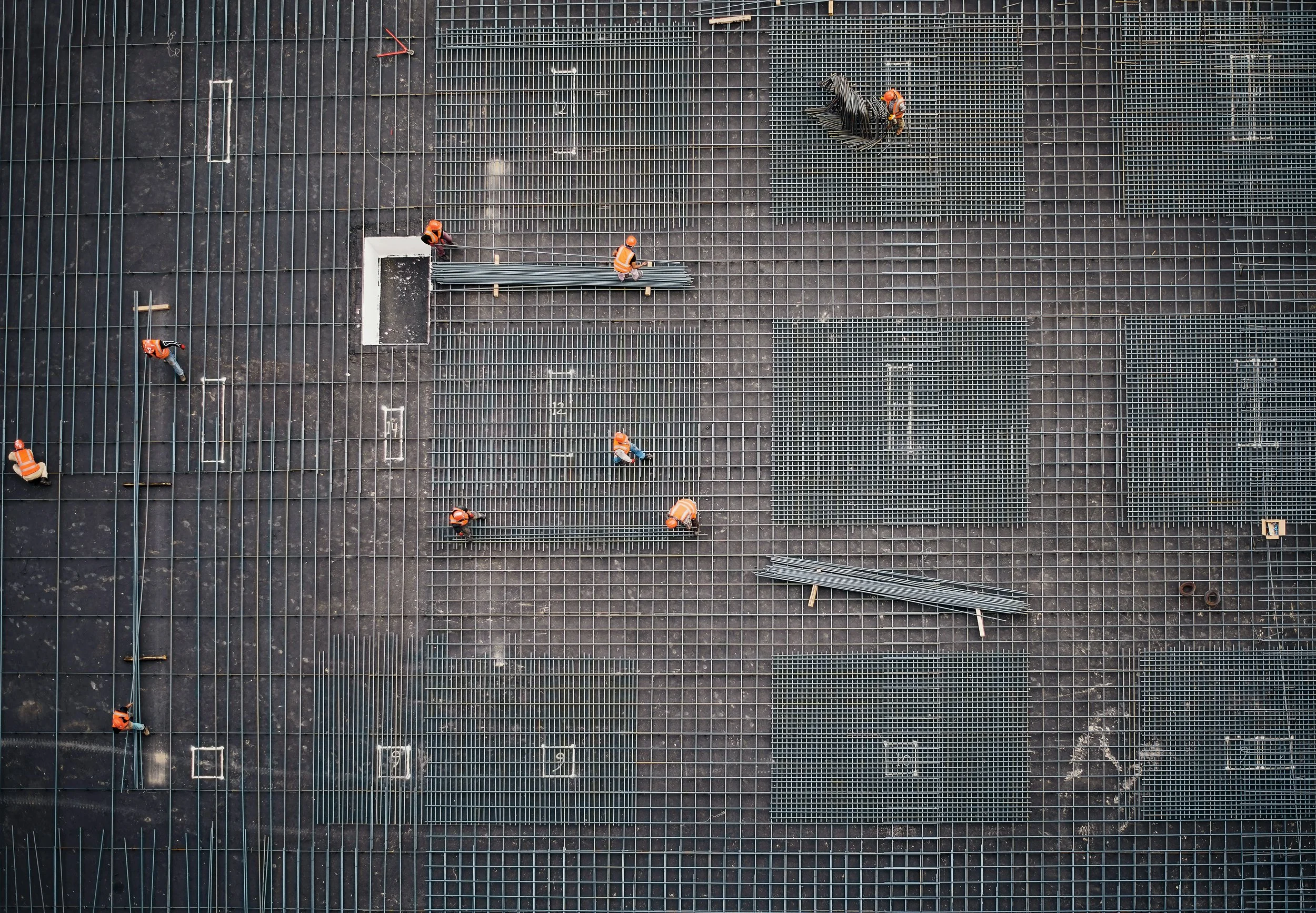 Construction workers install steel grates on a building's roof, viewed from above.
