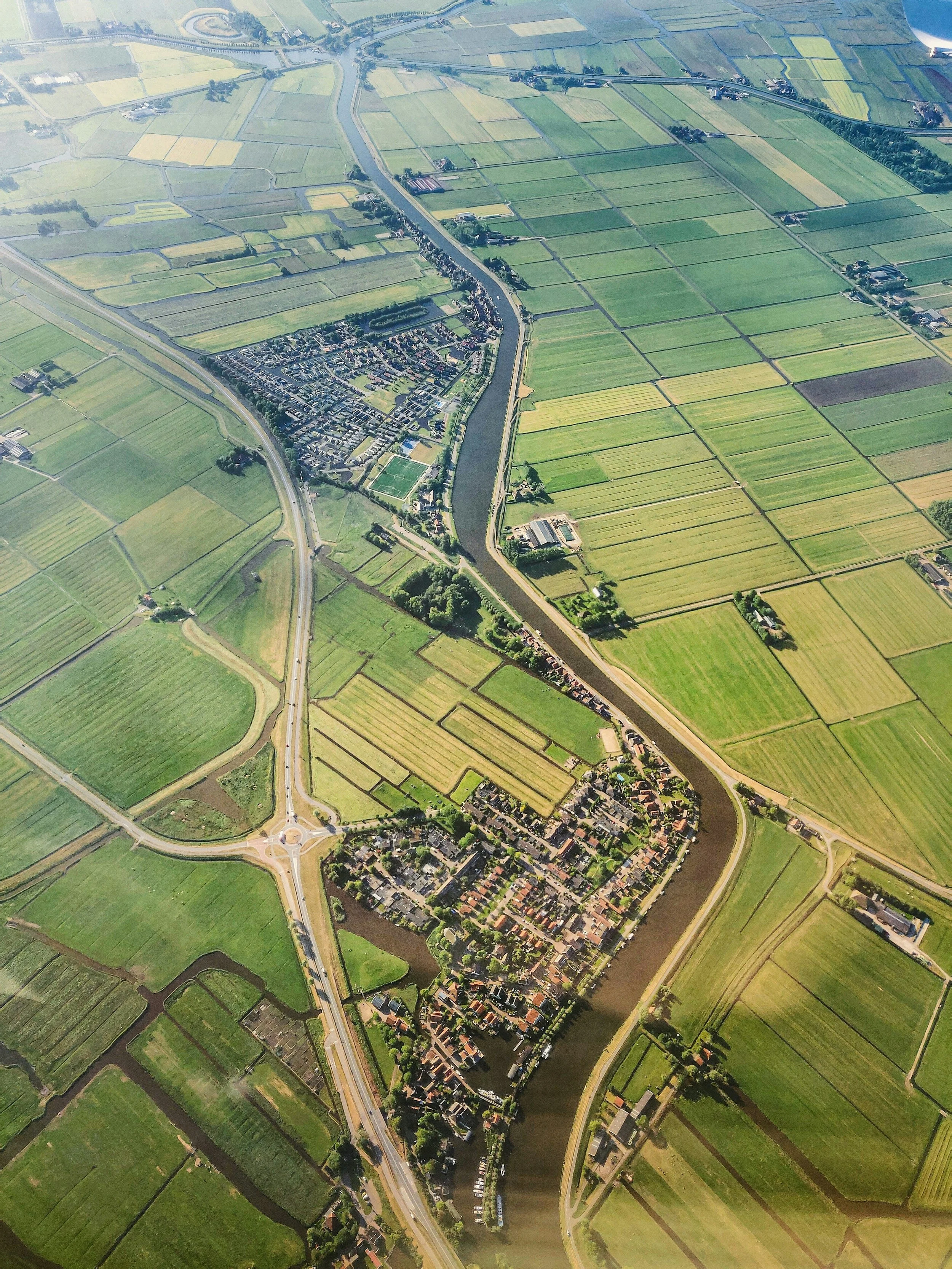 An aerial view of a small town with a river running through it, surrounded by green agricultural fields and farmland.