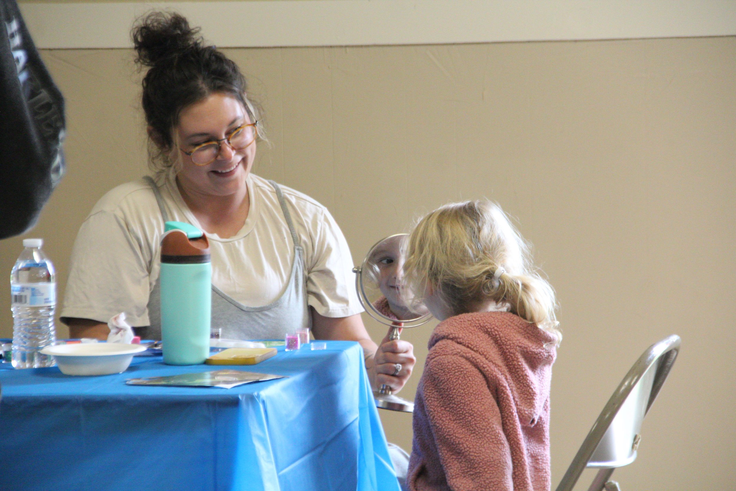 A volunteer helps a child with face painting at a community event