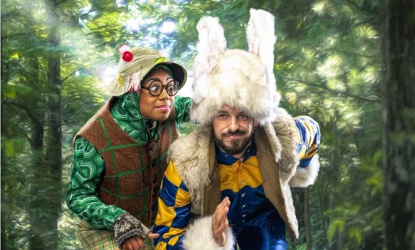 A man dressed as a Christmas elf, with antlers, a red and white striped bow tie, and holiday accessories, holding a sledgehammer, standing in front of a festive backdrop with the words "DUB SHOW".