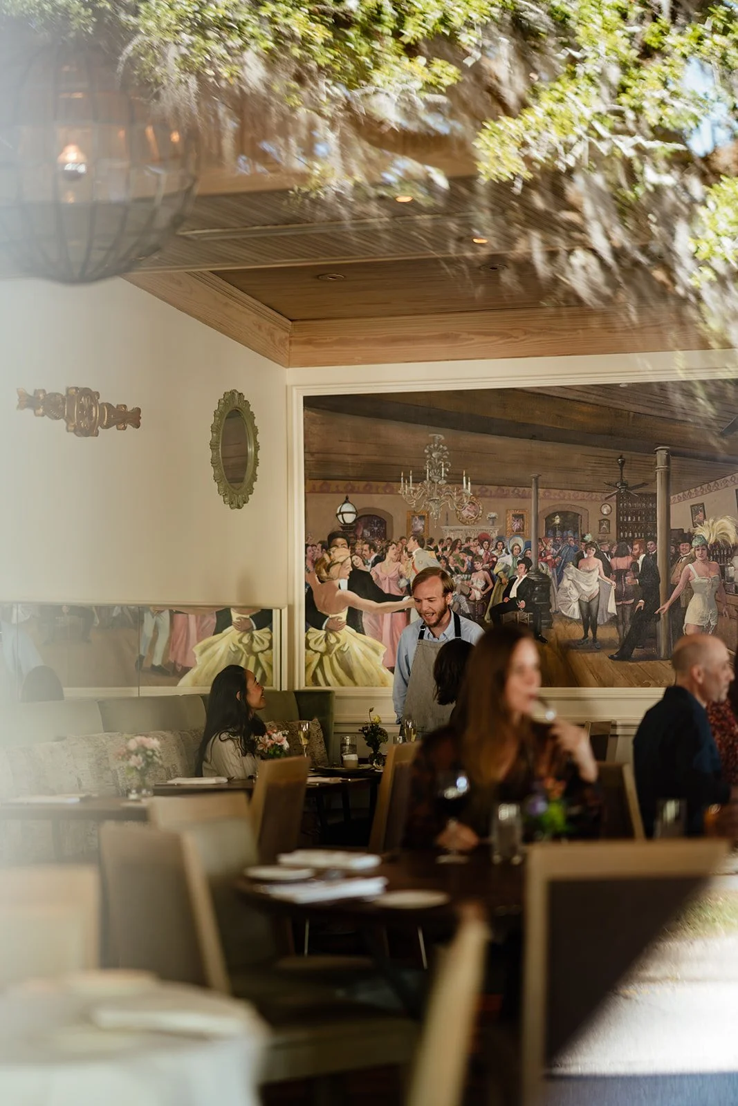 People dining inside a restaurant with a large mural of a vintage dance scene on the wall.