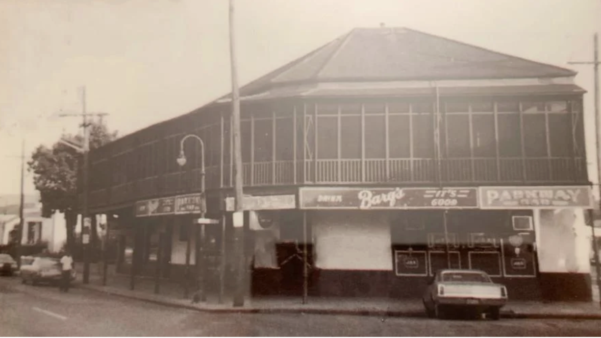 Historical black and white photo of Ralph's on the Park in 1985 when it opened as Tavern on the Park with a wooden balcony, a pharmacy on the ground floor, and vintage cars parked outside. 