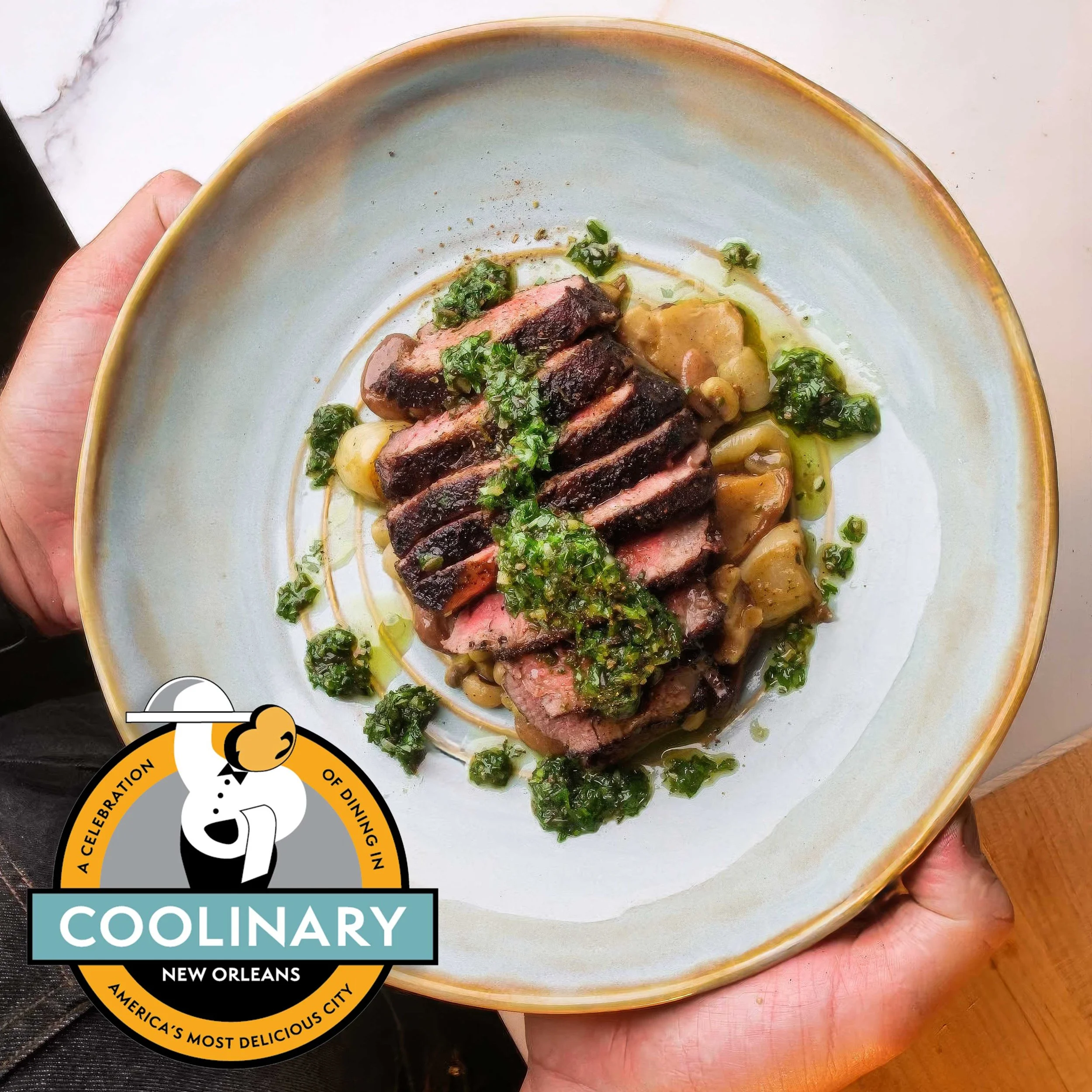 Sliced medium-rare steak over beans and roasted vegetables, topped with bright green herb sauce, served on a large ceramic plate.