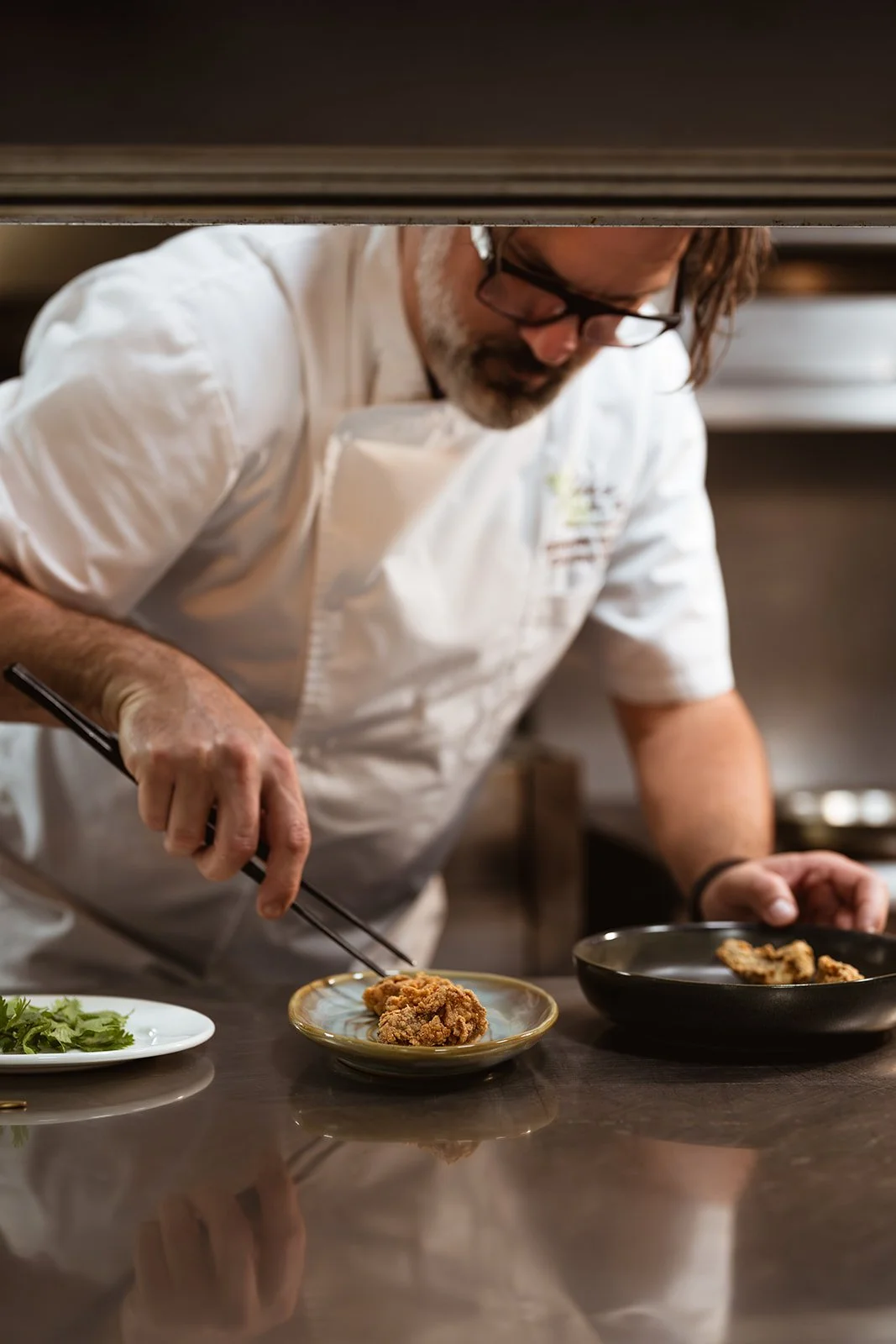 Chef placing fried oysters on a plate in a professional kitchen.