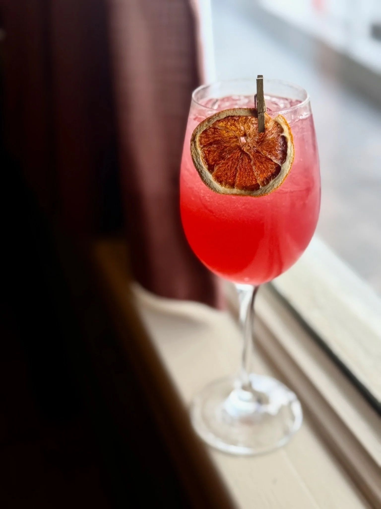 Ceramic tiki mug with a face design, featuring pink floral decorations around the top, and a straw in the mug, set against a blurred outdoor background.
