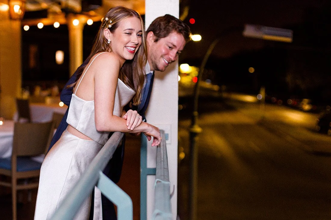 A happy couple leaning on a balcony railing at night, smiling and enjoying each other's company.