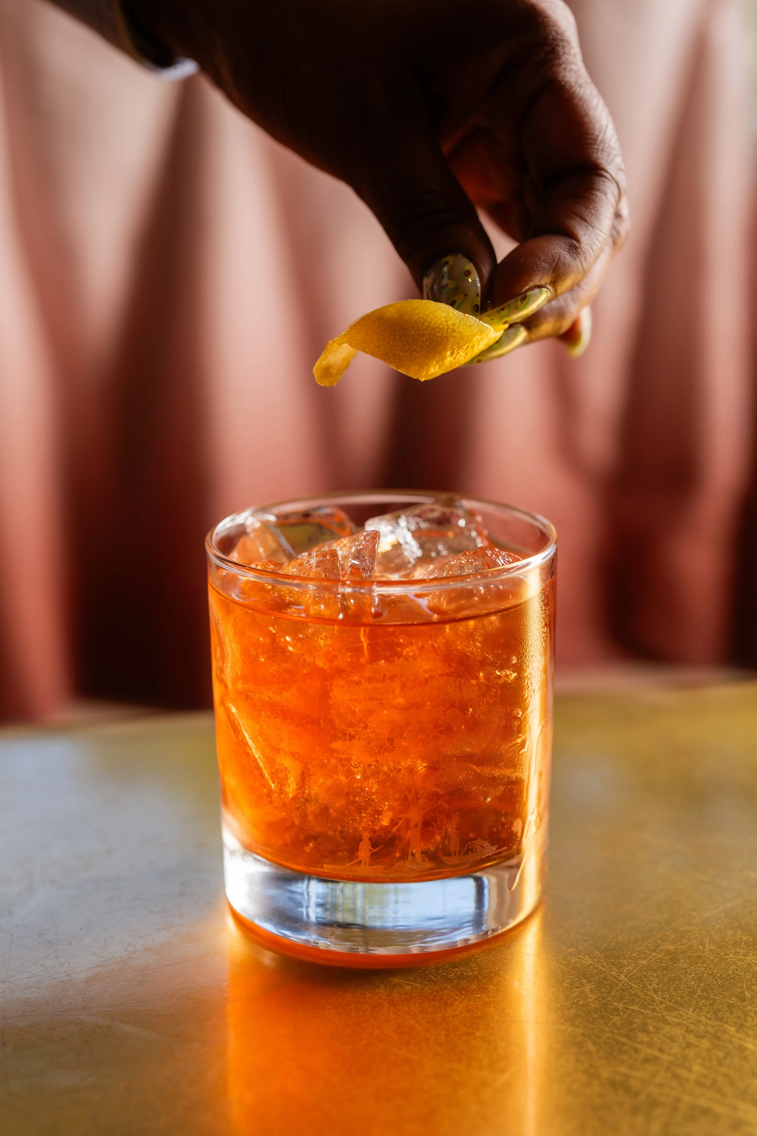 Ceramic tiki mug with a face design, featuring pink floral decorations around the top, and a straw in the mug, set against a blurred outdoor background.