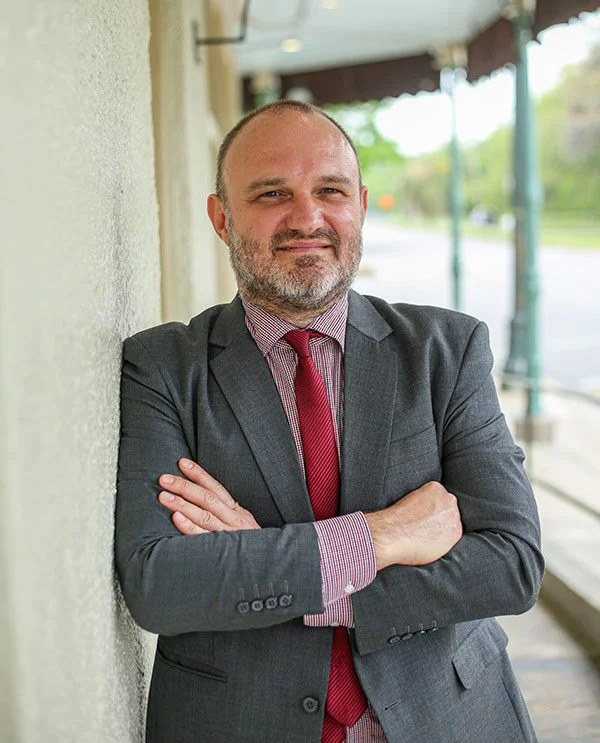 Man in a gray suit with red tie leaning against a wall outdoors