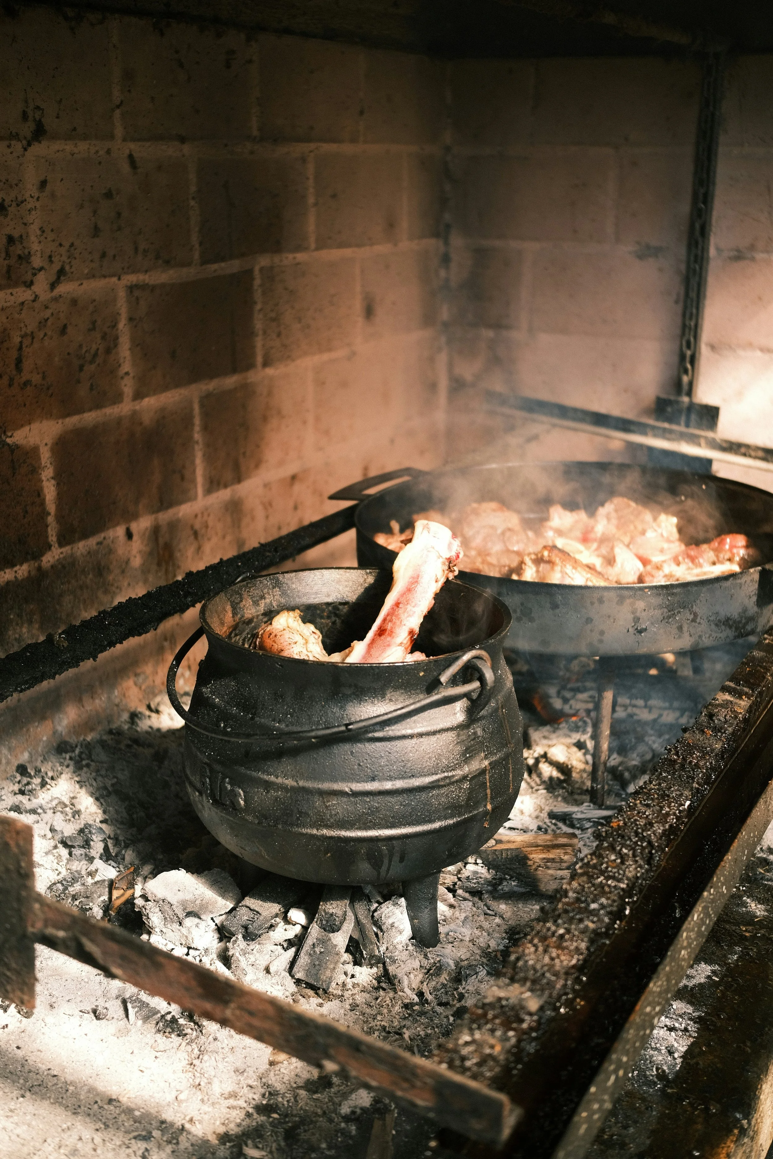 Cooking meat over an open fire in cast iron pots inside a brick oven.