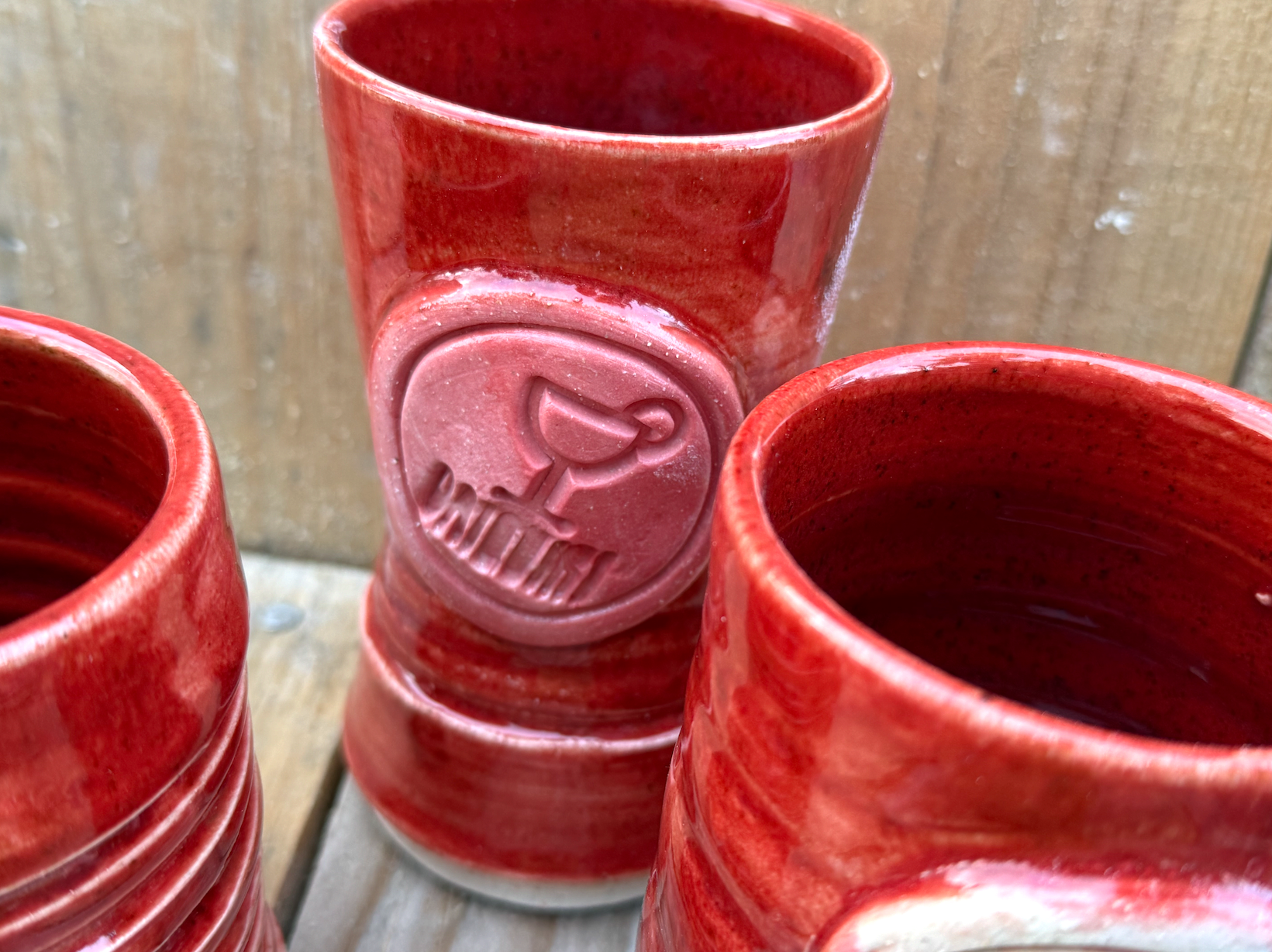 Red ceramic mug with a raised logo featuring a stylized duck and the word 'QUACK' on a wooden surface.